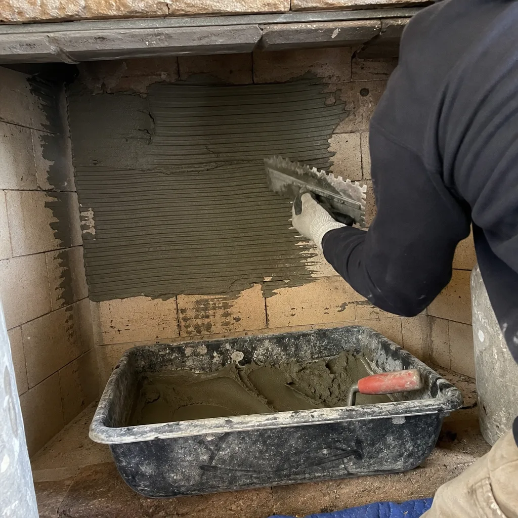 Professional contractor applying mortar to fireplace brick wall with notched trowel